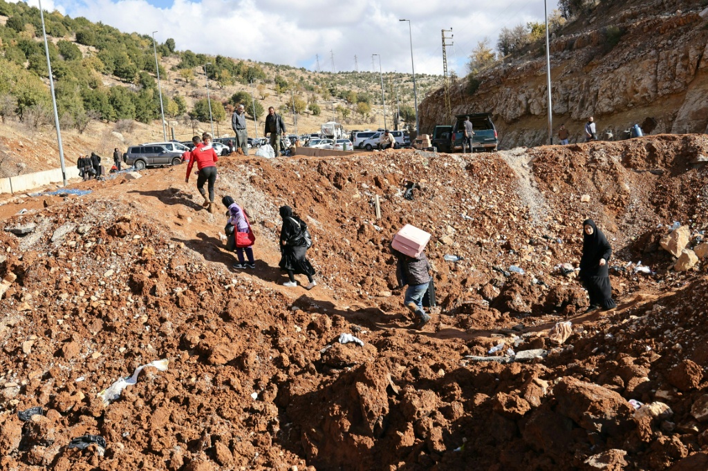    أهالي فارون من القصف الإسرائيلي في لبنان يجتازون حفرة ناجمة عن غارة إسرائيلية في منطقة المصنع على الجانب اللبناني من الحدود مع سوريا، في 20 تشرين الثاني/نوفمبر 2024 (أ ف ب)   