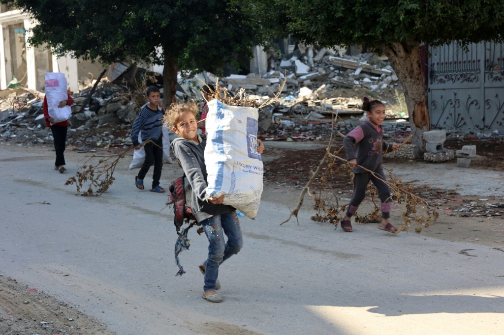 أطفال فلسطينيون يحملون الحطب إلى منازلهم في جباليا في 20 نوفمبر/تشرين الثاني (أ ف ب)   