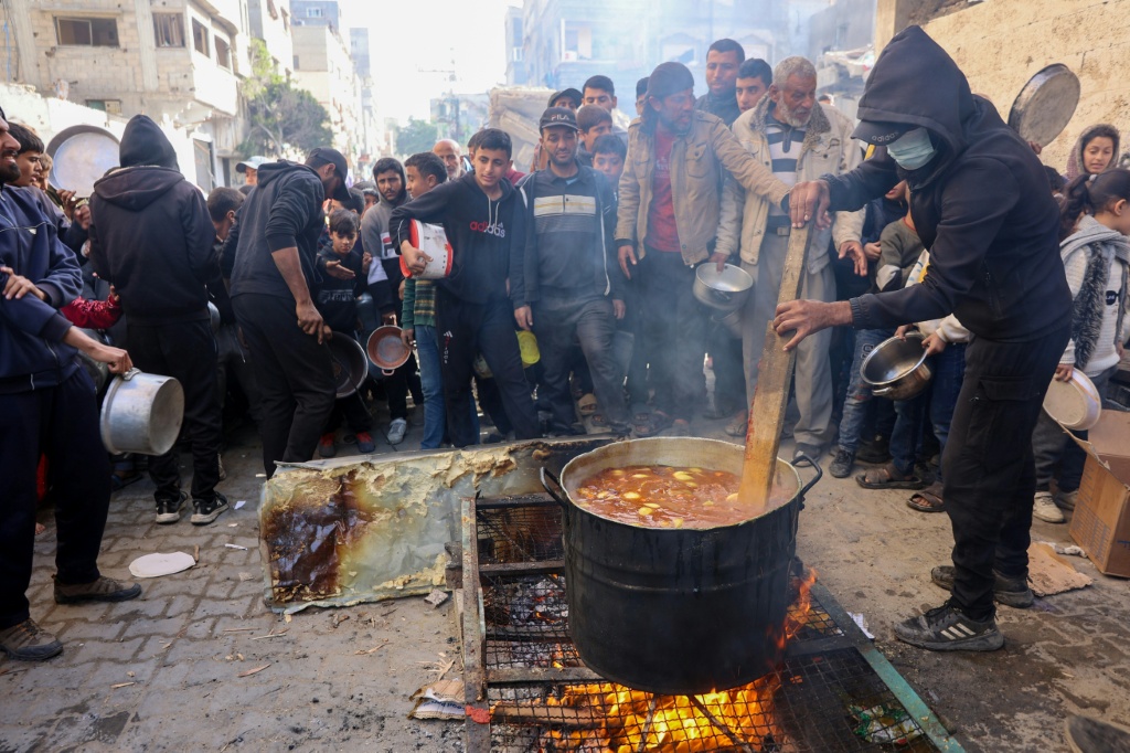    متطوع يحرك الطعام فيما ينتظر فلسطينيون للحصول على وجبات توفرها منظمات مساعدة إنسانية في مخيم الشاطئ للاجئين قرب مدينة غزة في 26 كانون الأول/ديسمبر 2024 (أ ف ب)   