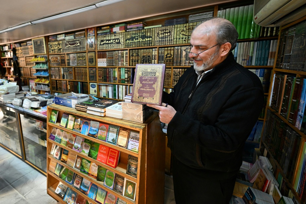 بائع كتب يعرض كتابًا قيل إنه تم حظره أثناء حكم الرئيس السوري المخلوع بشار الأسد (أ ف ب)   