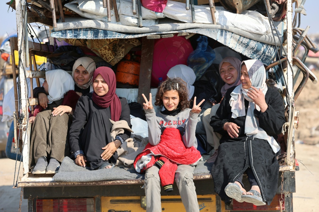 فلسطينيون نازحون يجلسون في مؤخرة شاحنة بينما يتجه الناس من الجنوب إلى الأجزاء الشمالية من قطاع غزة، على طريق صلاح الدين في وسط غزة، في 29 كانون الثاني/يناير 2025 (أ ف ب)   
