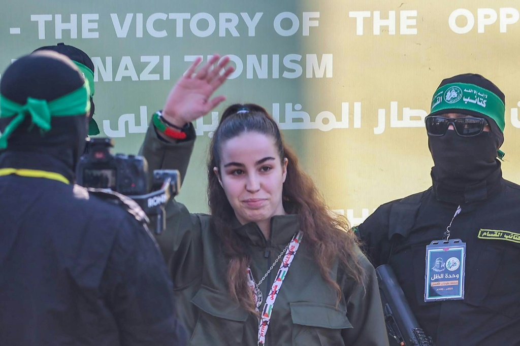 تلوح الجندية الإسرائيلية أجام بيرغر بيدها بينما يرافقها مسلحو حماس إلى المسرح لتسليمها لممثلي الصليب الأحمر كجزء من عملية تبادل الأسرى الثالثة بموجب وقف إطلاق النار في غزة. (أ ف ب)   