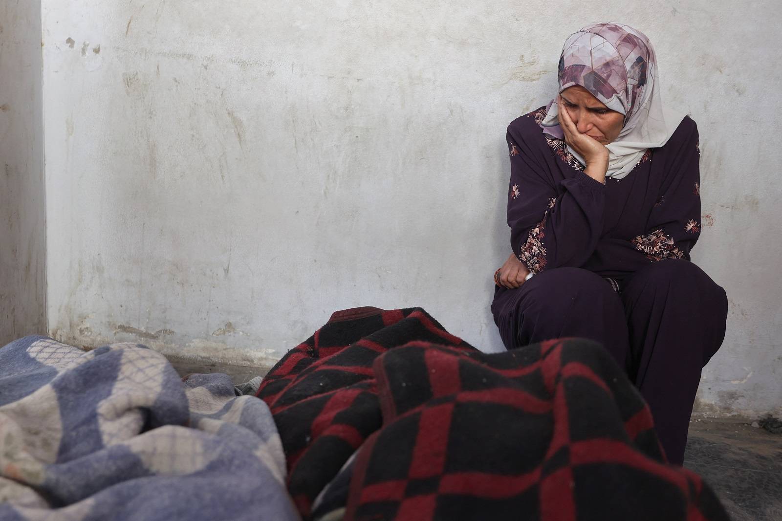 امرأة تجلس بالقرب من جثث ملفوفة بالبطانيات في مشرحة المستشفى المعمداني بمدينة غزة (أ.ف.ب)