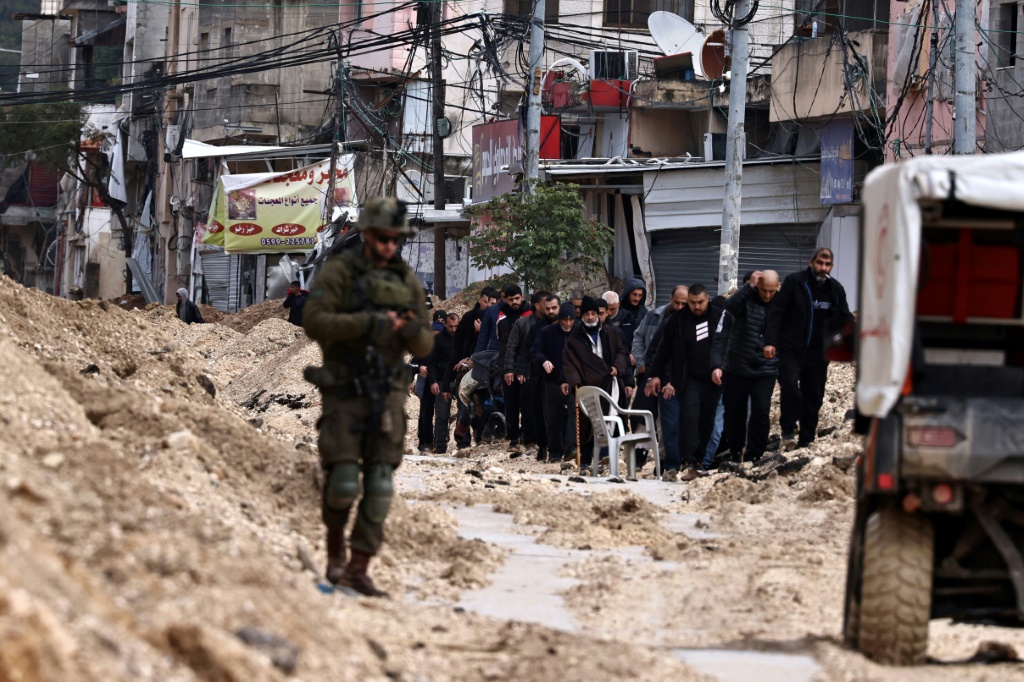 فلسطينيون يغادرون مخيم نور شمس قس الضفة الغربية المحتلة تحت نظر جندي إسرائيلي في العاشر من شباط/فبراير 2025 (ا ف ب)   