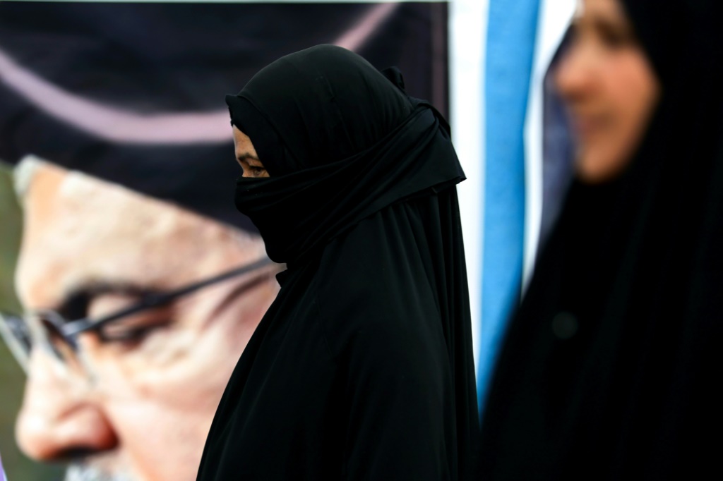 امرأة شيعية تمشي قرب صورة للأمين العام السابق لحزب الله حسن نصرالله، خلال مسيرة نحو مرقد الإمام الكاظم في بغداد في 23 كانون الثاني/يناير 2025 (ا ف ب)   