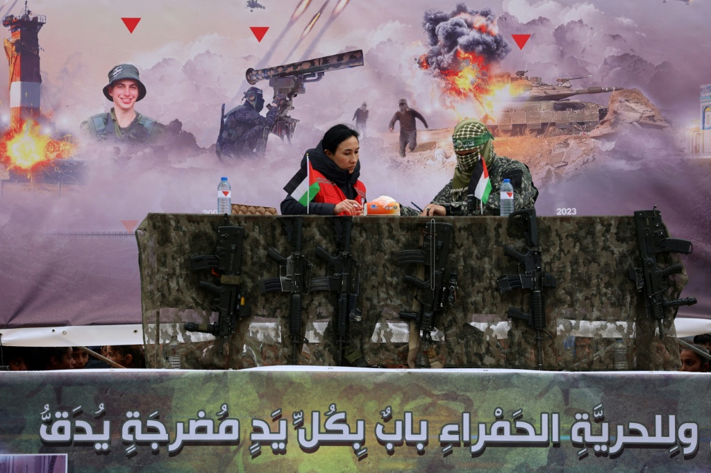 ممثلة الصليب الأحمر الدولي توقع وثائق مع أحد مقاتلي حماس على منصة في موقع تسليم رهينتين إسرائيليين في رفح جنوب قطاع غزة، كجزء من عملية التبادل السابعة في 22 شباط/فبراير 2025 (أ ف ب)   