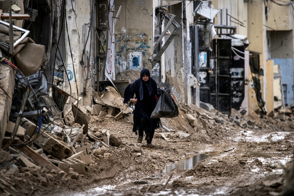 نازحة فلسطينية تحمل أمتعتها لدى مرورها من أمام أبنية مدمرة في مخيم جنين في الضفة الغربية المحتلة بتاريخ 24 شباط/فبراير 2025 (أ ف ب)   
