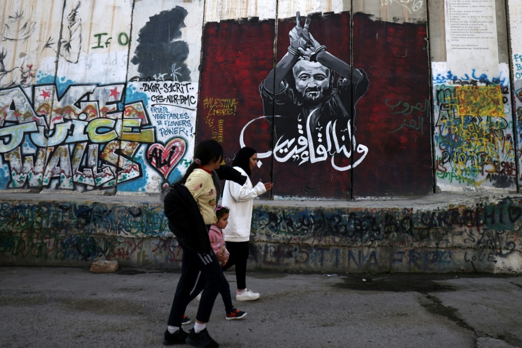 شباب فلسطينيون يسيرون بجانب الجدار الفاصل بين إسرائيل والضفة الغربية المحتلة، أمام لوحة جدارية تصور السياسي الفلسطيني المسجون مروان البرغوثي، في بيت لحم في 26 شباط/فبراير 2025 (أ ف ب)   