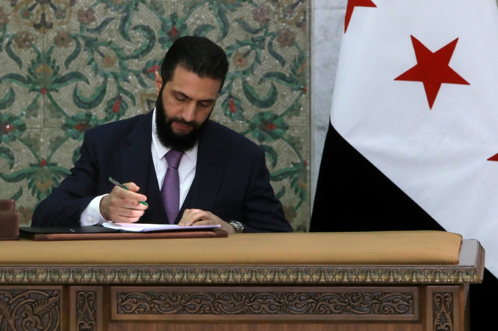 الرئيس السوري الانتقالي أحمد الشرع يوقع مسودة الإعلان الدستوري للمرحلة الانتقالية في دمشق في 13 آذار/مارس 2025 (أ ف ب)