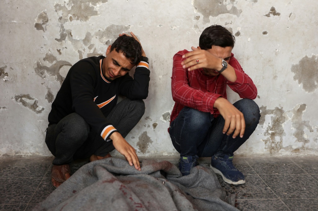  فلسطينيون بجوار جثة ملفوفة ببطانية في مستشفى الأهلي في السابع من أيار/مايو 2025، بعد غارة إسرائيلية على مدينة غزة (أ ف ب)   