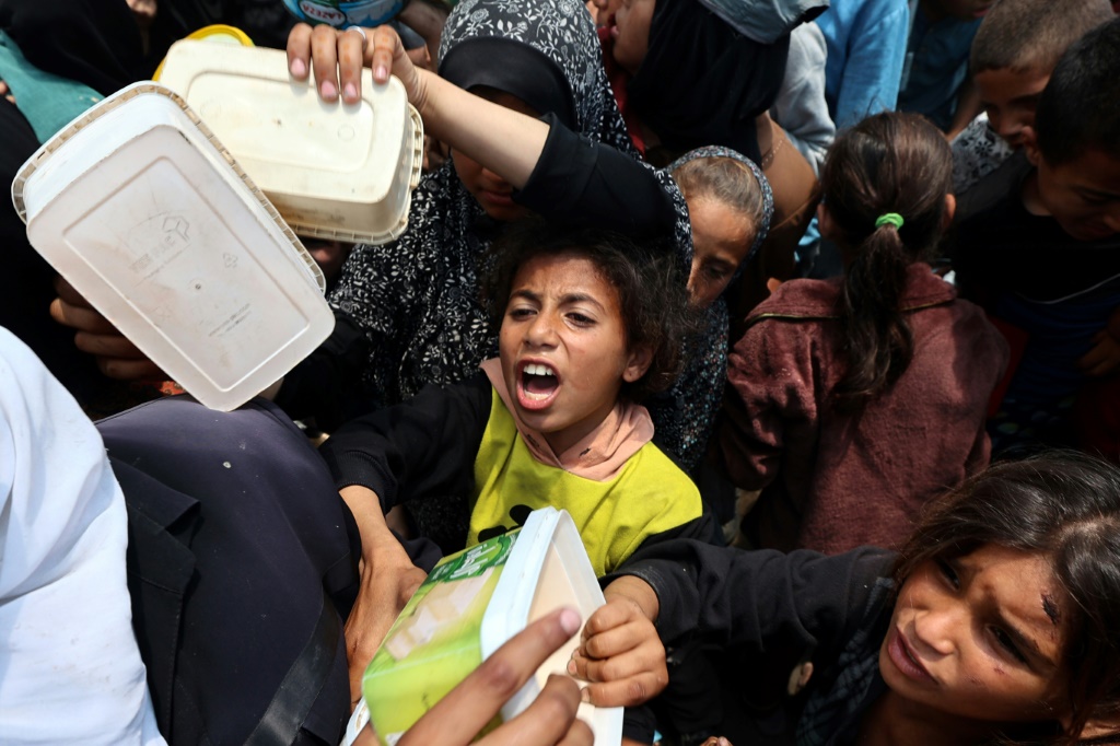  أطفال فلسطينيون يتدافعون للحصول على طبق من الطعام في مخيم النصيرات في وسط قطاع غزة في 21 أيار/مايو 2025 (أ ف ب)