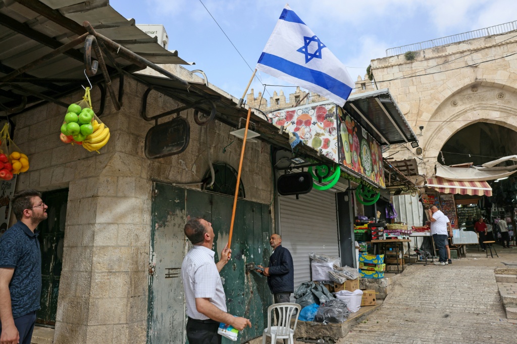 في البلدة القديمة بالقدس في 27 أيار/مايو 2025 رجل ينزل العلم الإسرائيلي عن متجر يملكه فلسطيني يحاول قص قفل متجره الذي تعرض للتخريب من قبل متطرفين يهود في اليوم السابق، خلال ذكرى احتلال الجيش الإسرائيلي للقدس الشرقية عام 1967 (ا ف ب)   