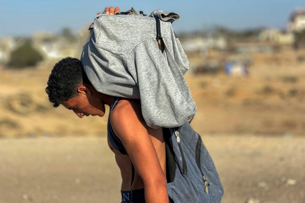    شاب فلسطيني يمشي حاملا على ظهره مساعدات من مؤسةس إغاثة مدعومة اميركيا في غرب رفح في حنوب قطاع غزة في 27 أيار/مايو 2025 (أ ف ب)