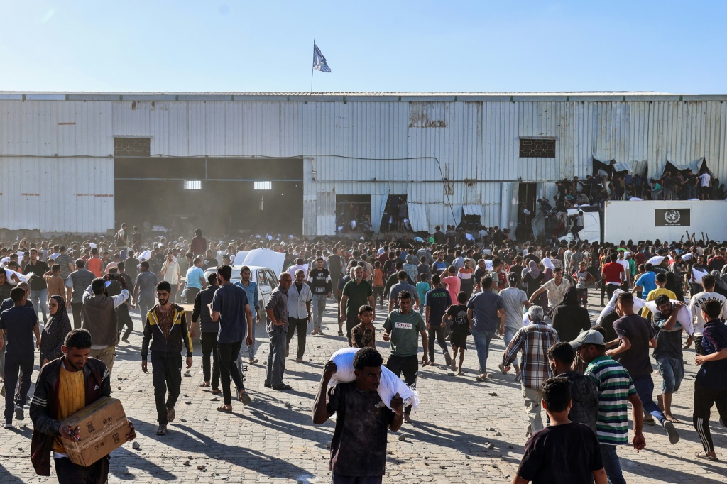 نازحون فلسطينيون يحملون أكياس مساعدات غذائية بعد اقتحامهم مستودعا لبرنامج الأغذية العالمي في دير البلح بوسط قطاع غزة، في 28 أيار/مايو 2025 (أ ف ب)