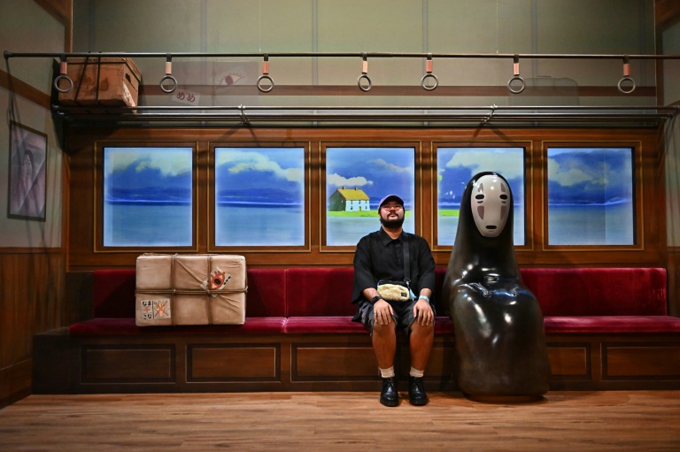 رجل يجلس بجوار شخصية No Face من فيلم "Spirited Away" من إنتاج ستوديو جيبلي خلال عرض إعلامي لمعرض "عالم الرسوم المتحركة في ستوديو جيبلي بانكوك" قبل الافتتاح العام في العاصمة التايلاندية في 29 حزيران/يونيو 2023 (أ ف ب)