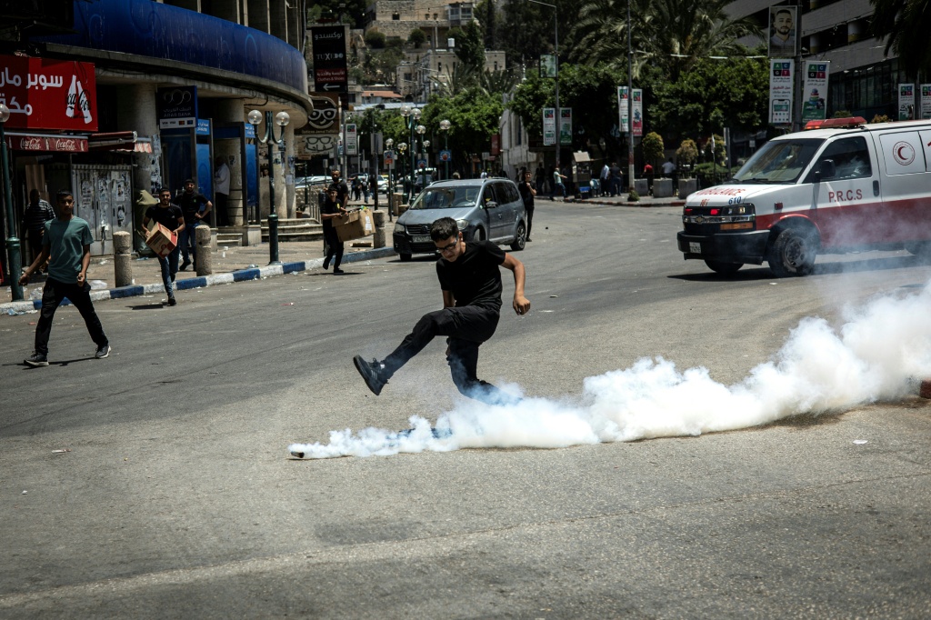 شاب فلسطيني يركل قنبلة غاز مسيل للدموع بعد أن أطلقتها قوات الاحتلال الإسرائيلي على المتظاهرين في مدينة نابلس بالضفة الغربية المحتلة في 10 حزيران/يونيو 2025 (أ ف ب)