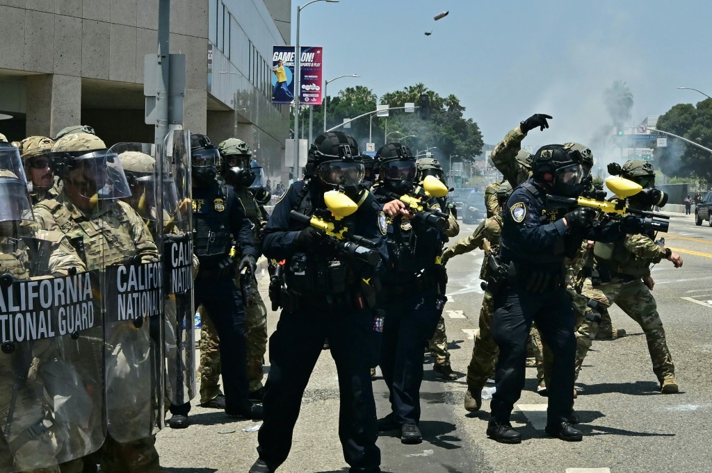 متظاهر يلوح براية تحمل العلمين الأميركي والمكسيكي ويقف أمام عناصر من الحرس الوطني لكاليفورنيا، خلال احتجاجات على ترحيل مهاجرين في لوس أنجليس في 12 حزيران/يونيو 2025 (ا ف ب)
