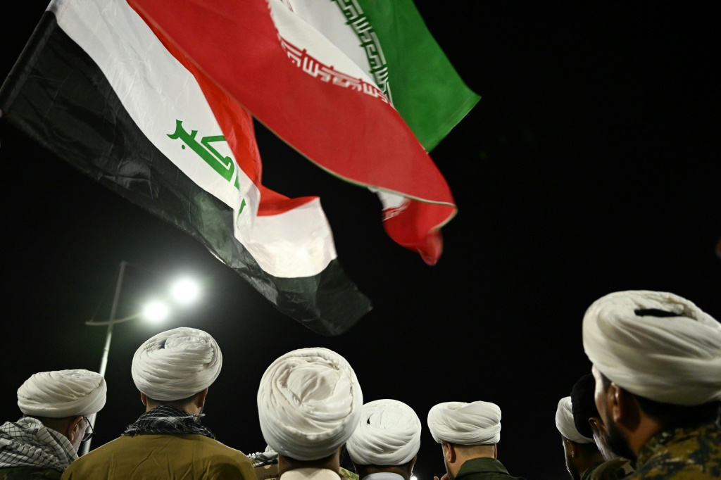 رجال دين شيعة بلباس عسكري يرفعون العلمَين العراقي والإيراني في تجمّع في مدينة البصرة بجنوب العراق في 18 حزيران/يونيو 2025 للتنديد بالضربات الإسرائيلية على إيران (أ ف ب)