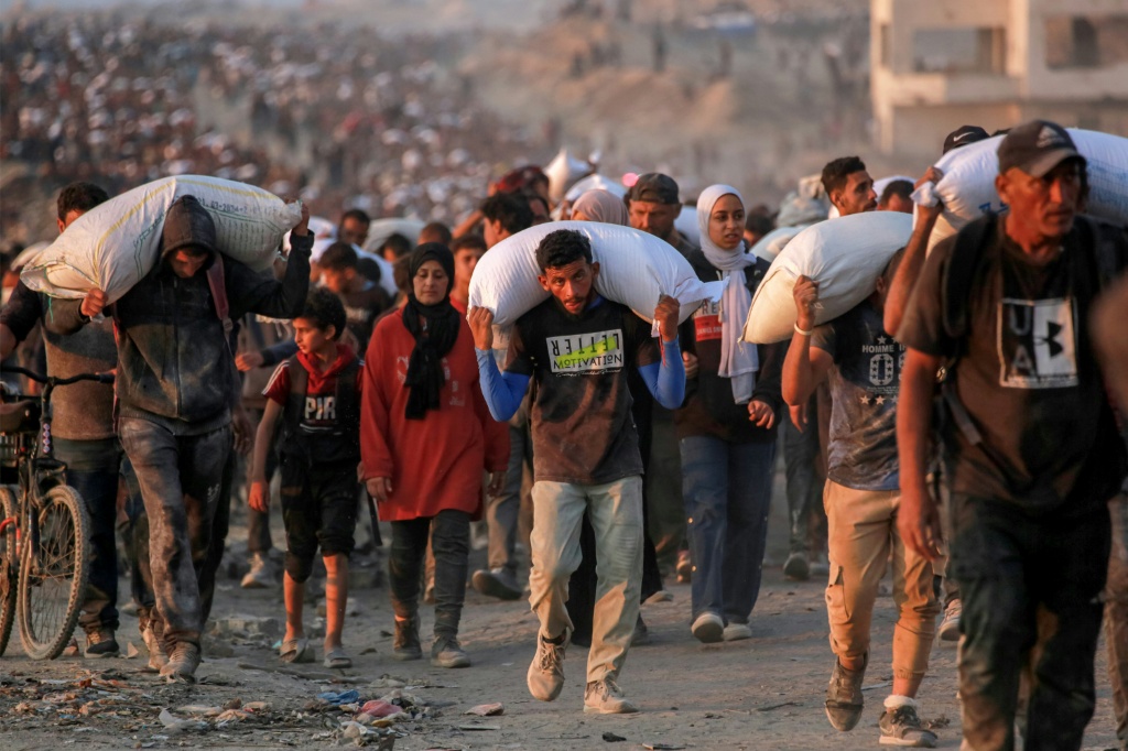 فلسطينيون يحملون أكياس طحين في شارع الرشيد في جباليا في قطاع غزة في 17 حزيران/يونيو 2025 (ا ف ب)