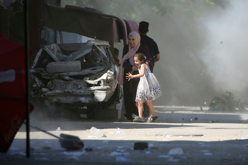 أم فلسطينية وابنتها تهرعان للاحتماء أثناء غارة إسرائيلية على مخيم البريج وسط قطاع غزة في 4 تموز/يوليو 2025 (أ ف ب)