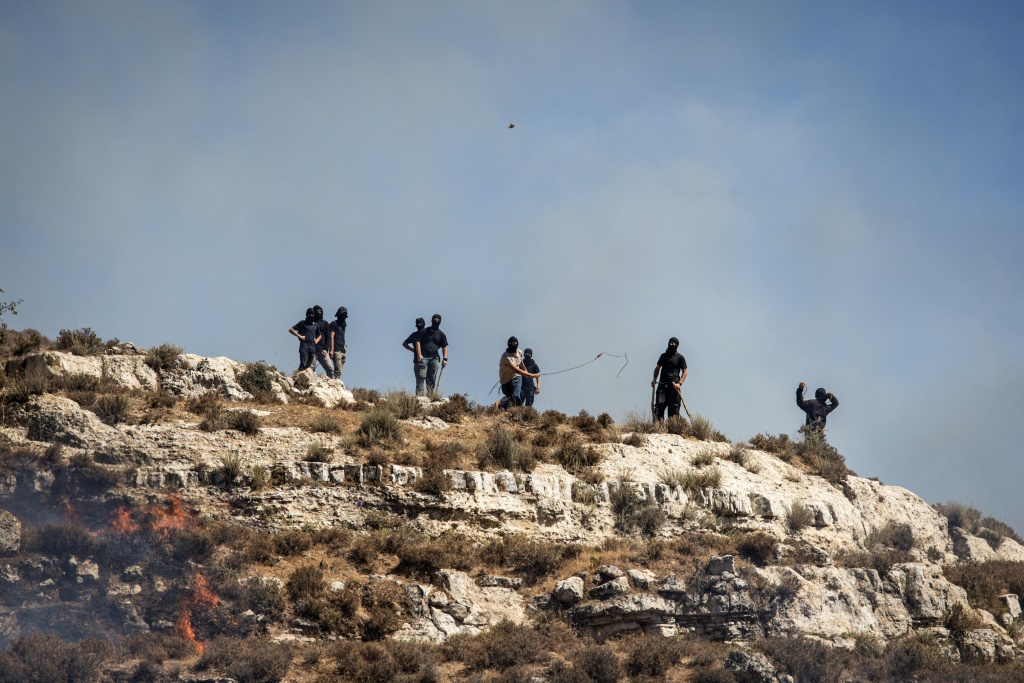 مستوطنون إسرائيليون ملثمون يرشقون الفلسطينيين بالحجارة من أعلى تلة في بلدة سنجل بالضفة الغربية المحتلة في 4 تموز/يوليو 2025 (ا ف ب)