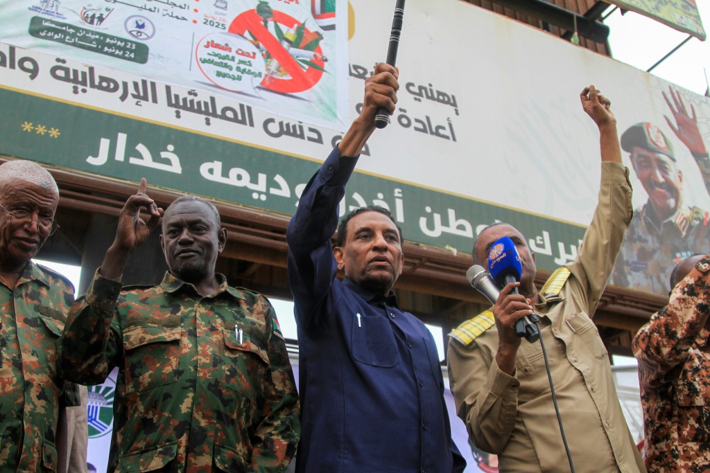 كامل إدريس (وسط الصورة)، المسؤول السابق في الأمم المتحدة الذي عينه الزعيم الفعلي للسودان عبد الفتاح البرهان في أيار/مايو رئيسا للوزراء، يخاطب الناس والمقاتلين المحليين الذين يدعمون الجيش السوداني خلال زيارة إلى أم درمان في 19 تموز/يوليو 2025 (أ ف ب)