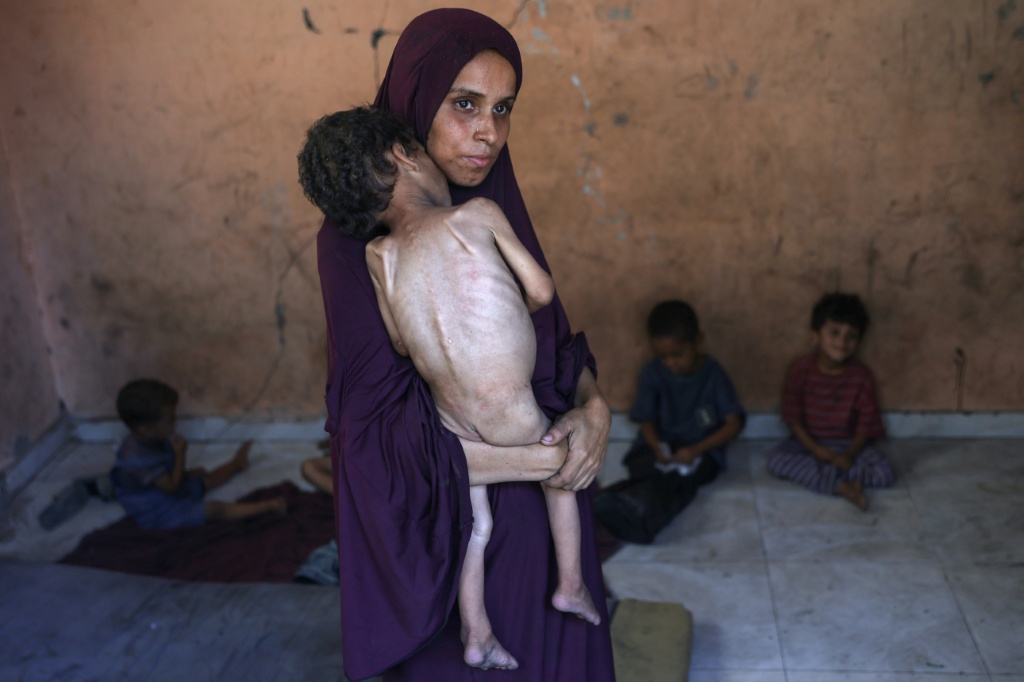 نعيمة هي أم فلسطينية تبلغ من العمر 30 عامًا تحمل ابنها يزن البالغ من العمر عامين والذي يعاني من سوء التغذية في منزلهما المدمر في مخيم الشاطئ للاجئين، غرب مدينة غزة، في 23 تموز/يوليو 2025. (أ ف ب)