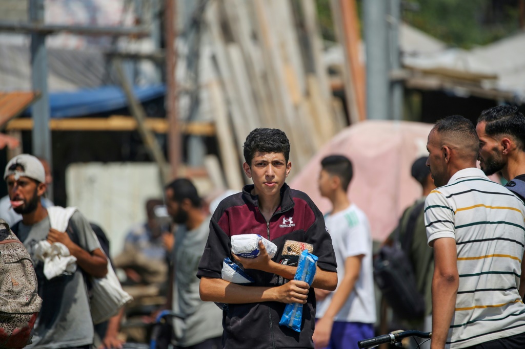نازحون فلسطينيون يحملون مواد غذائية حصلوا عليها عند نقطة توزيع في وسط قطاع غزة، في 26 تموز/يوليو 2025 (أ ف ب)