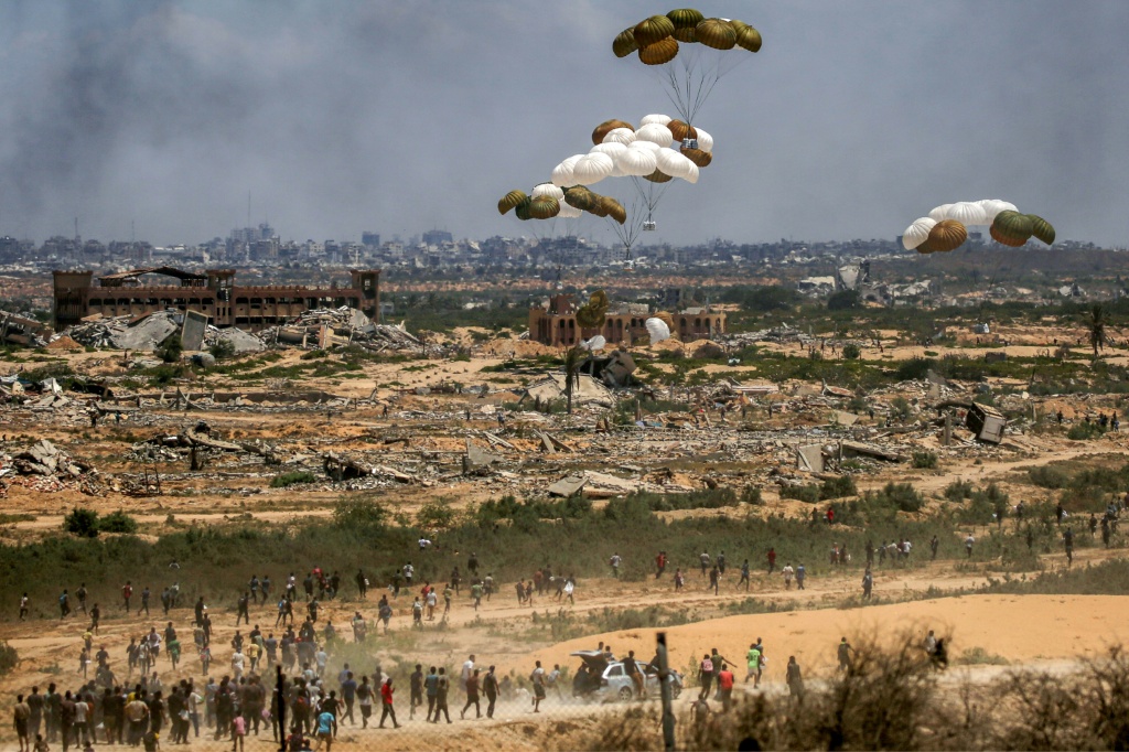 فلسطينيون يسرعون إلى موقع إنزال رزم المساعدات بالمظلات بعد إسقاطها من طائرة عسكرية فوق النصيرات في وسط قطاع غزة في 5 آب/أغسطس 2025 (أ ف ب)