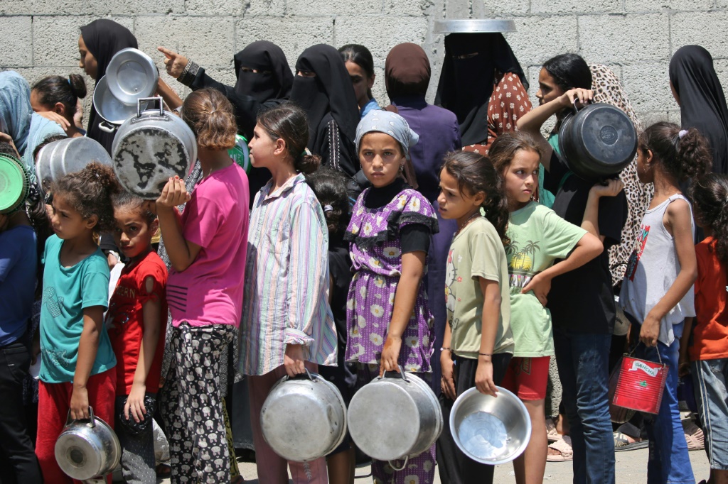 أطفال فلسطينيون ينتظرون الحصول على وجبات طعام في مركز توزيع في مخيم النصيرات وسط قطاع غزة 18 آب/أغسطس 2025 (أ ف ب)