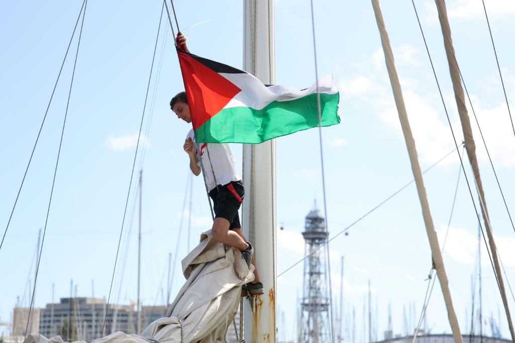 عضو في أسطول الصمود العالمي يضع العلم الفلسطيني على أحد القوارب التي تحمل مساعدات إنسانية ونشطاء يستعدون للمغادرة إلى غزة، في برشلونة في 30 آب/أغسطس 2025 (أ ف ب)