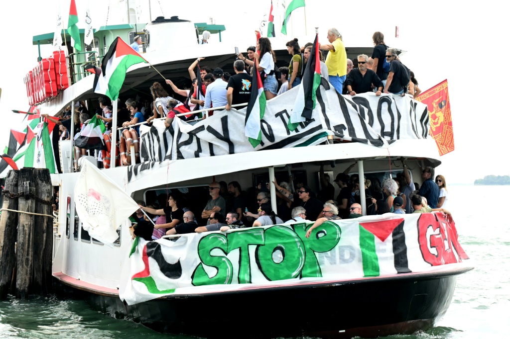 يستقلون عبارة ملوحين بالاعلام الفلسطينية تمهيدا للمشاركة في تظاهرة تضامنا مع غزة على هامش مهرجان البندقية السينمائي في 30 آب/اغسطس 2025 (أ ف ب)