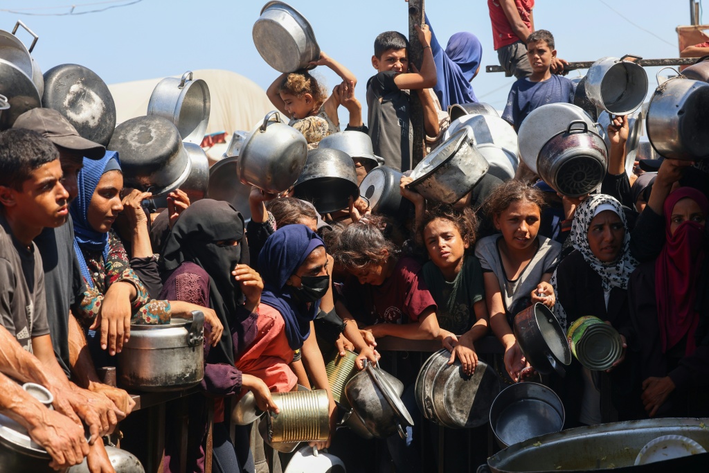 نساء وأطفال فلسطينيون ينتظرون الحصول على حصص غذائية من مطبخ خيري في خان يونس جنوب قطاع غزة في 27 آب/أغسطس 2025 (أ ف ب)