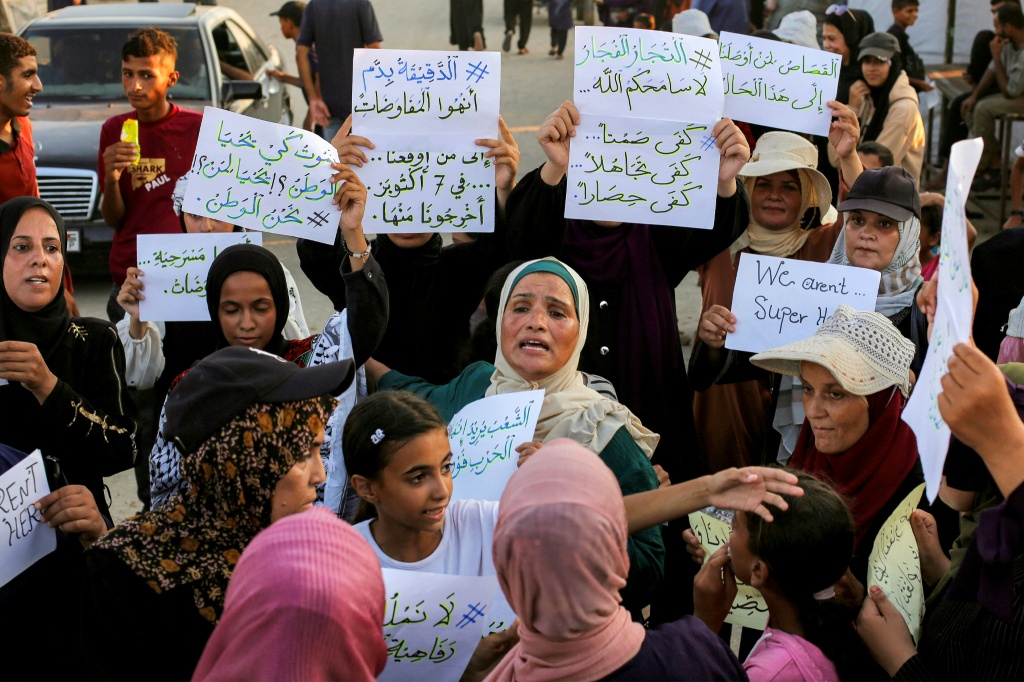 نساء وأطفال يحملون لافتات أثناء مشاركتهم في مسيرة صامتة ضد الحرب والجوع في منطقة المواصي شرق خان يونس في جنوب قطاع غزة في 26 تموز/يوليو 2025 (أ ف ب)