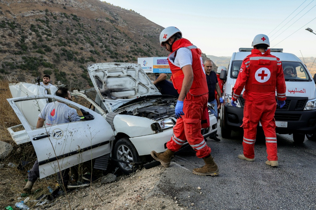 مسعفان من الصليب الاحمر اللبناني امام سيارة تعرضت لضربة اسرائيلية في منطقة مرجعيون بجنوب لبنان في 20 ايلول/سبتمبر 2025 (أ ف ب)