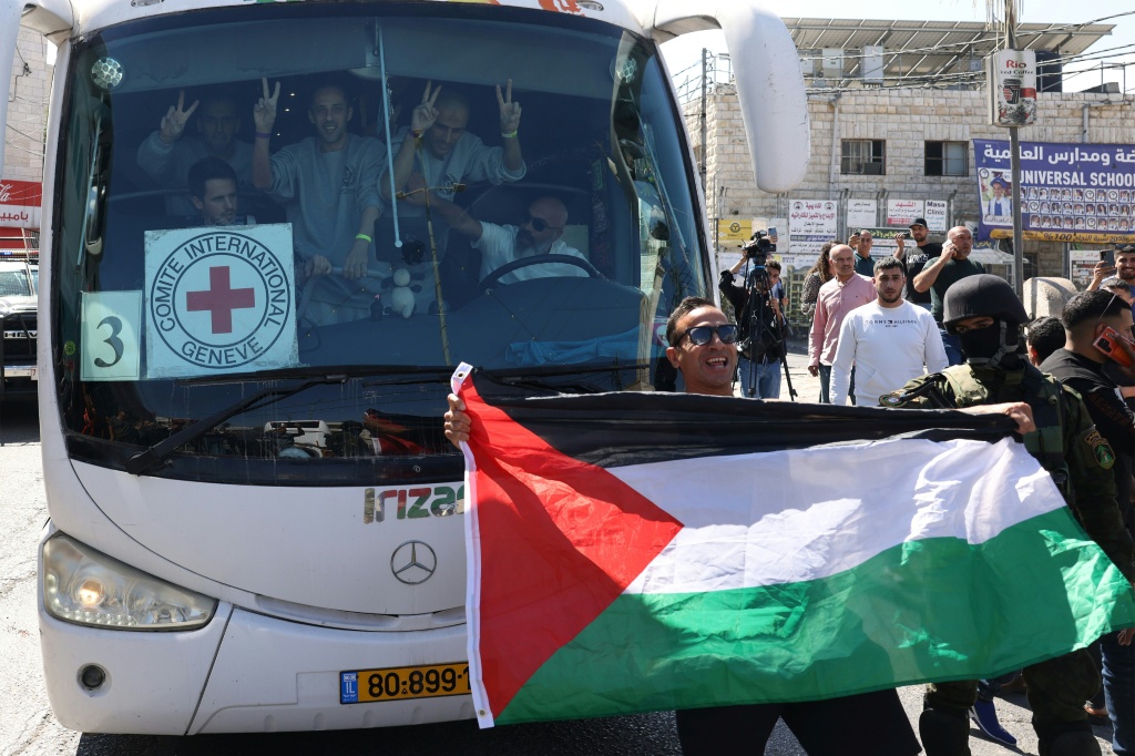 رجل يرفع العلم الوطني الفلسطيني أمام حافلة تقل معتقلين أفرجت عنهم إسرائيل من سجن عوفر العسكري الواقع بين رام الله وبيتونيا في الضفة الغربية المحتلة في 13 تشرين الأول/أكتوبر 2025 (أ ف ب)
