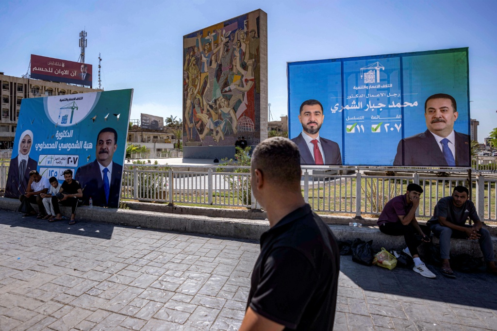 أشخاص يمرون من أمام لافتات للمرشحين والكتل المتنافسين في انتخابات تشرين الثاني/نوفمبر التشريعية في بغداد بتاريخ 3 تشرين الاول/أكتوبر 2025 (ا ف ب)