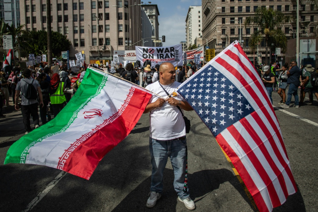 رجل يحمل علما إيرانيا وعلما أميركيا بالمقلوب أثناء تجمع مناهض للحرب على إيران في لوس أنجليس بتاريخ 7 حزيران/يونيو 2025 (ا ف ب)