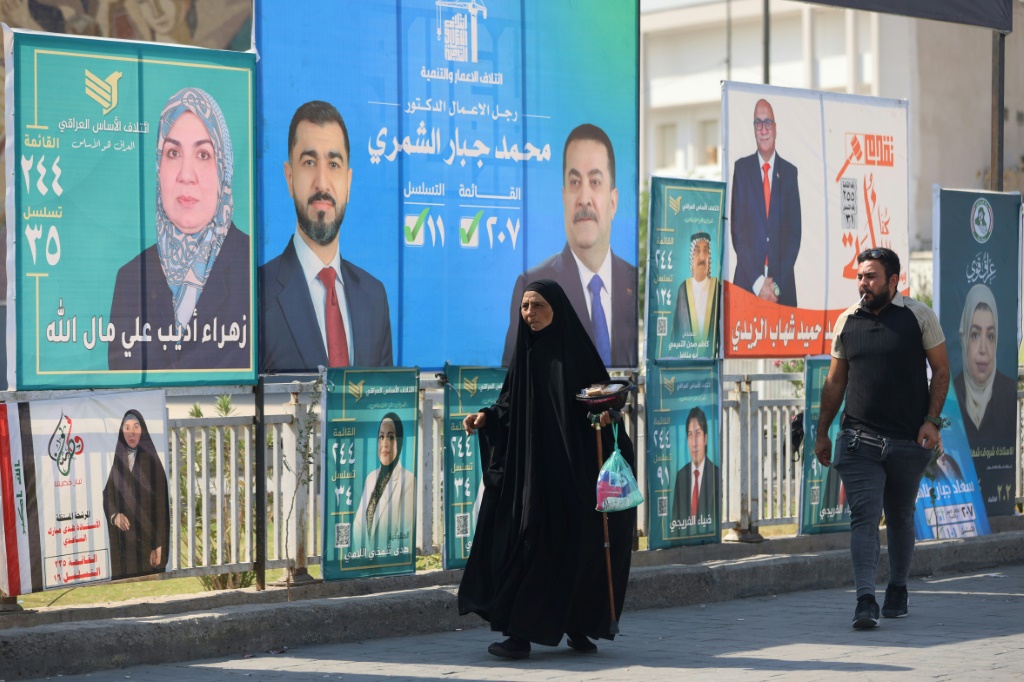 مارّة على طريق بجانب لافتات الحملة الانتخابية اللاقتراع التشريعي في وسط بغداد في 19 تشرين الأول/أكتوبر 2025 (ا ف ب) 