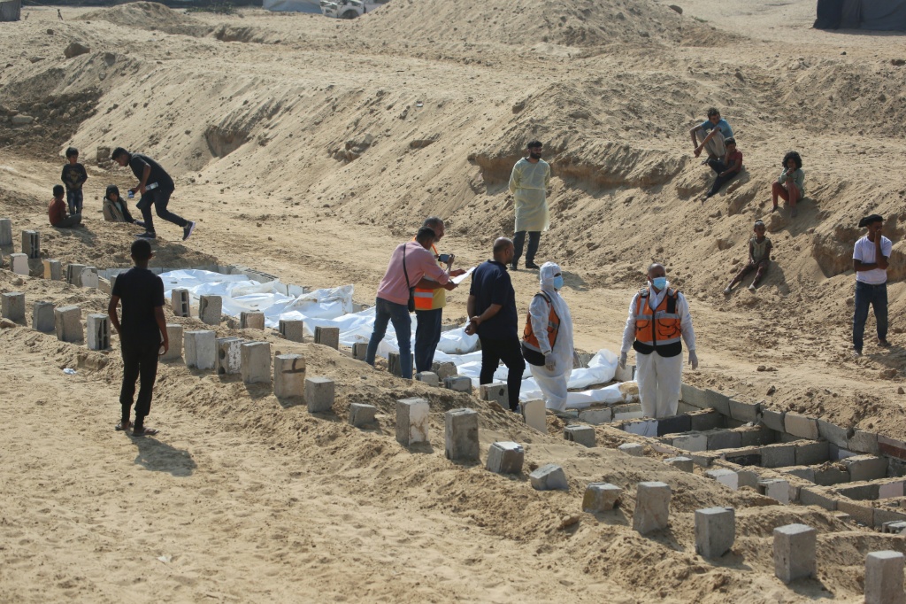 اطفال يراقبون تحضير مسعفين لتشييع جماعي لفلسطينيين في مقبرة بخان يونس جنوب قطاع غزة في العاشر من تشرين الثاني/نوفمبر 2025 (ا ف ب)