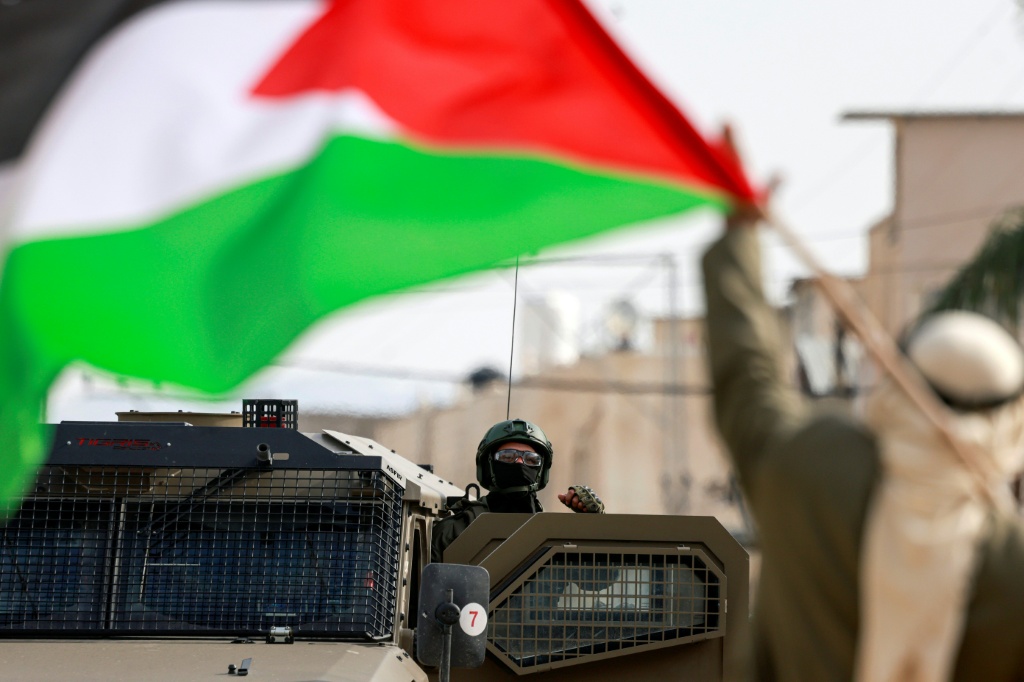 رجل يحمل العلم الفلسطيني بمواجهة جندي إسرائيل في مخيم نور شمس في الضفة بتاريخ 15 كانون الأول/ديسمبر 2025 (ا ف ب)