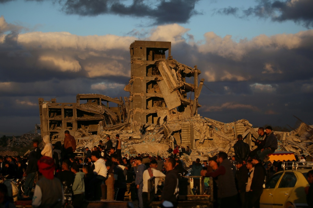 نازحون فلسطينيون يقفون بجوار منازل مدمرة في مخيم النصيرات بوسط قطاع غزة في 19 كانون الأول/ديسمبر 2025 (اف ب)