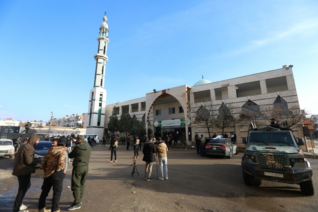 عناصر أمن وصحافيون خارج مسجد الإمام علي بن أبي طالب عقب انفجار داخل المسجد في حي وادي الذهب بمدينة حمص في 26 كانون الأول/ديسمبر 2025 (ا ف ب)