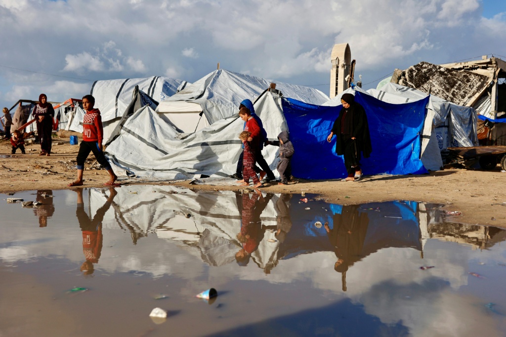 نازحون فلسطينيون قرب بركة كبيرة من مياه الأمطار تجمّعت إلى جوار خيام الإيواء، في مدينة غزة في 28 كانون الأول/ديسمبر 2025 (ا ف ب)