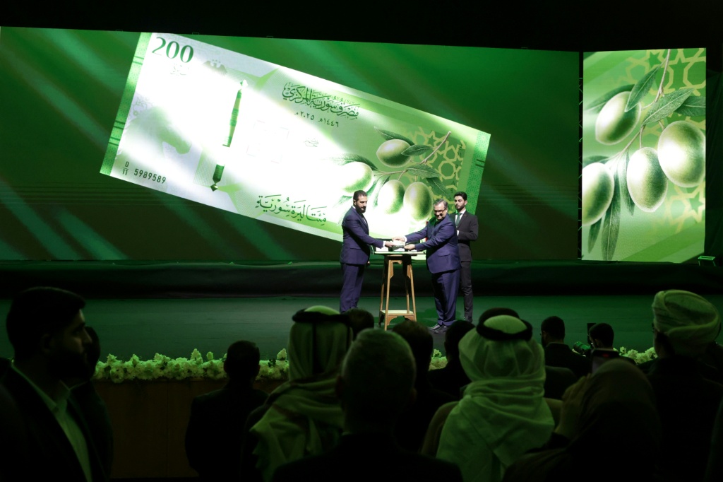 الرئيس السوري أحمد الشرع (يسار) وحاكم المصرف المركزي السوري عبد القادر الحصرية يعرضان ورقة مالية جديدة في قصر المؤتمرات في دمشق في 29 كانون الأول/ديسمبر 2025 (ا ف ب)