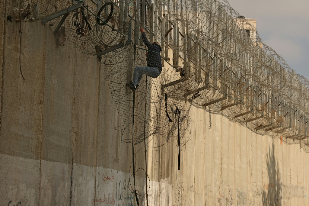 فلسطيني يستخدم حبلا ليتسلّق في 3 كانون الثاني/يناير 2026 في بيت حنينا بالقدس الشرقية، الجدار الفاصل الذي أقامته إسرائيل بين الضفة الغربية المحتلة والقدس. (ا ف ب)