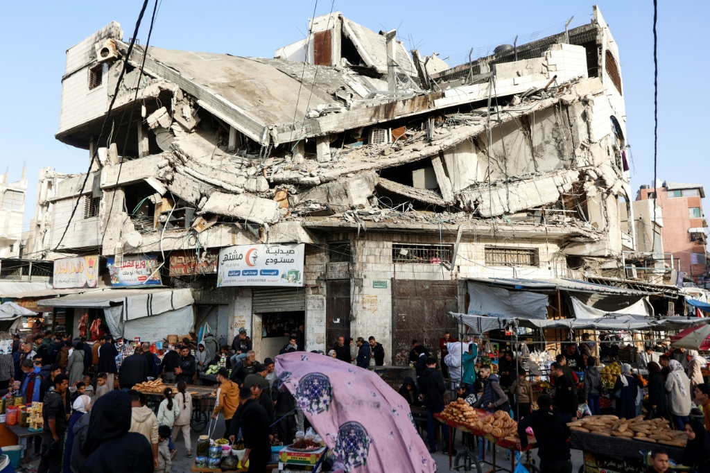 فلسطينيون يشترون طعاما من باعة تجمعوا أمام مبنى مدمر في مدينة غزة في 18 شباط/فبراير 2026 في أوّل أيام رمضان (ا ف ب)