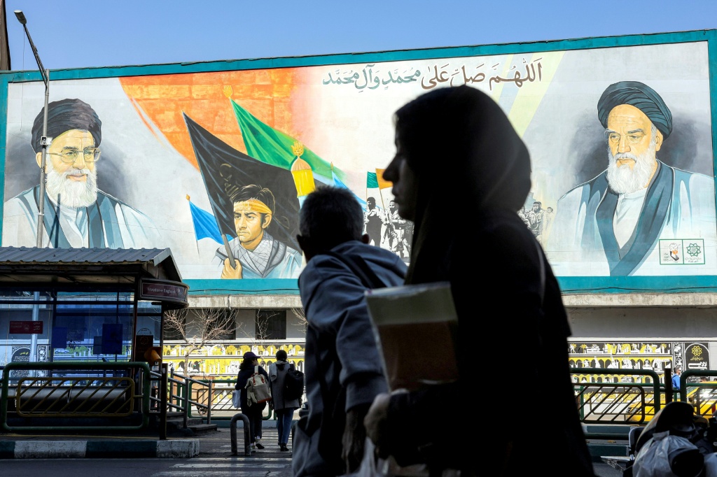 ايرانية تعبر امام ملصق كبير في طهران يحمل صورتي روح الله الخميني وعلي خامنئي في 21 شباط/فبراير 2026 (ا ف ب)