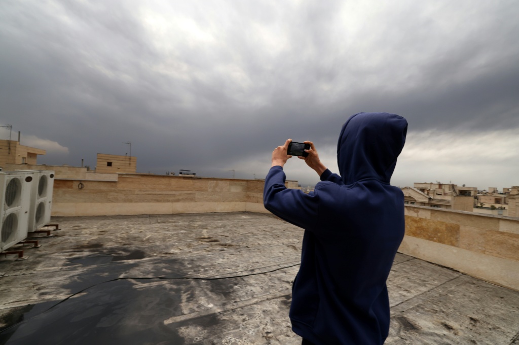 أحد سكان طهران يلتقط في 8 آذار/مارس 2026 صورا لسحابة الدخان الأسود من على سطح منزله المغطّى بالسخام بعد ضربات ليلية على مصفاة نفط (ا ف ب)