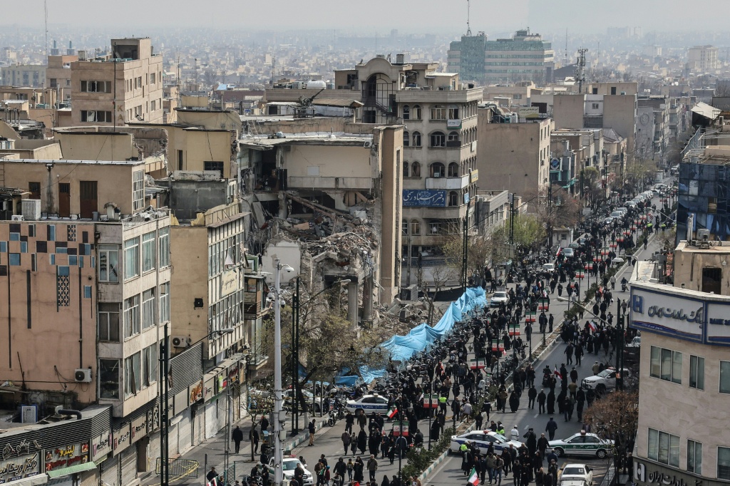 إيرانيون يمرون من أمام مبنى متضرر أثناء حضورهم جنازات قادة في الحرس الثوري وغيرهم ممن قتلوا في الحرب في ساحة انقلاب في طهران بتاريخ 11 آذار/مارس &nbsp;2026 (ا ف ب)